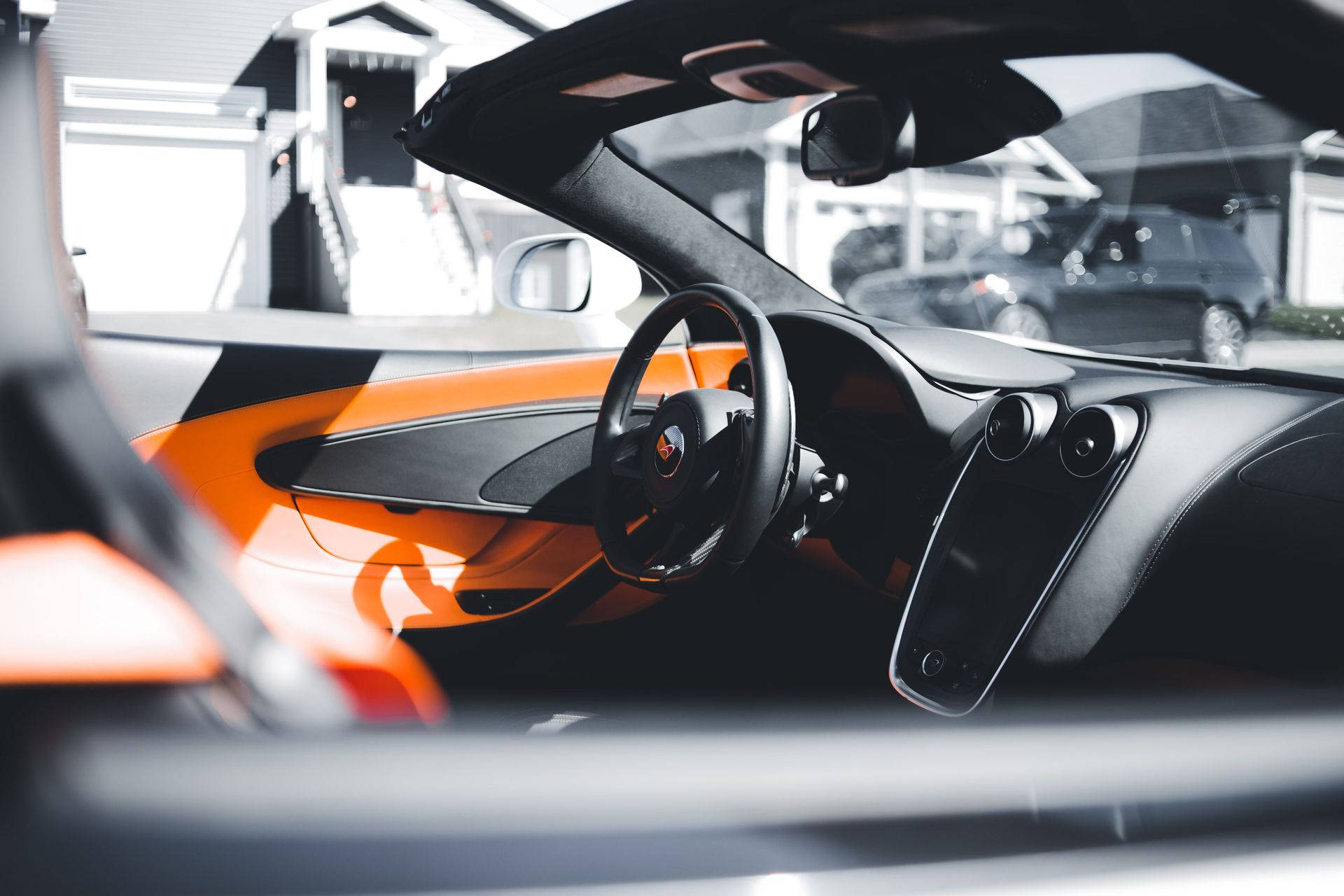 Interior of a sleek orange-and-black sports car, showing the steering wheel and dashboard in a showroom