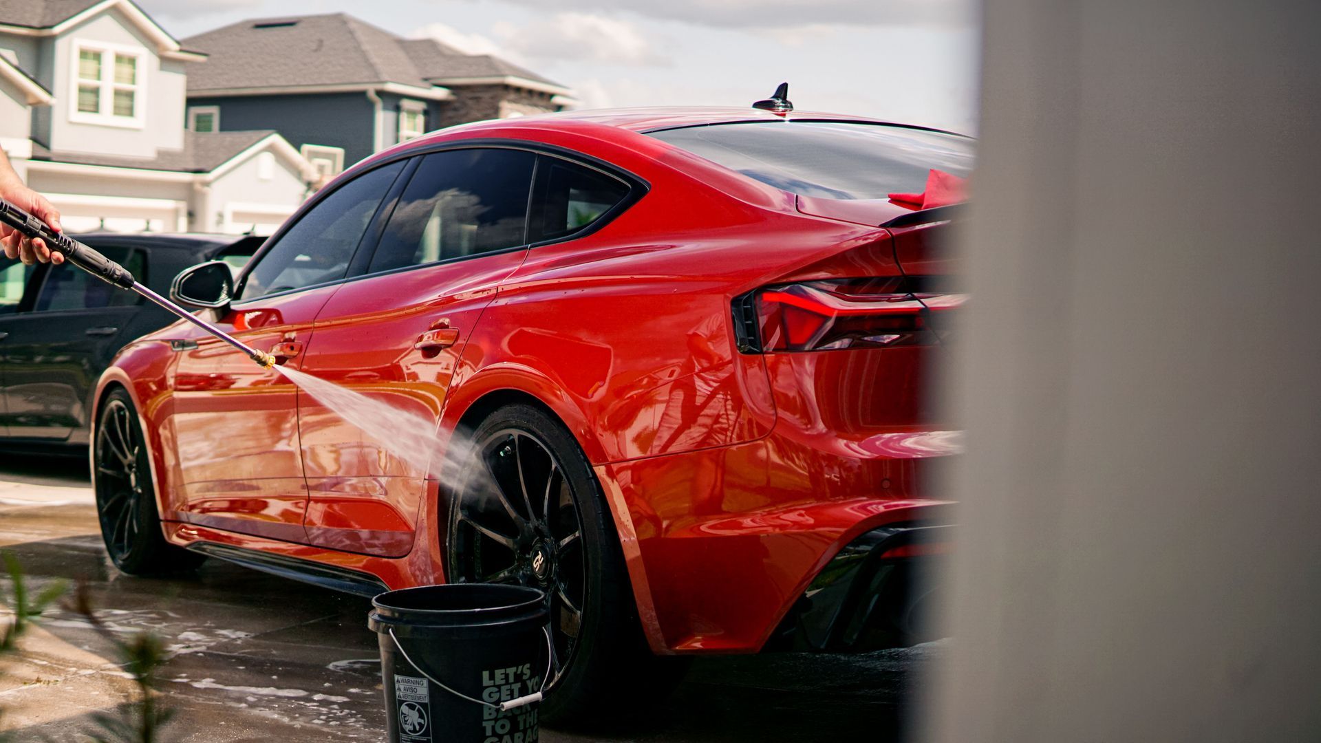 Red sports car being washed in a driveway, with soap suds and a bucket nearby.
