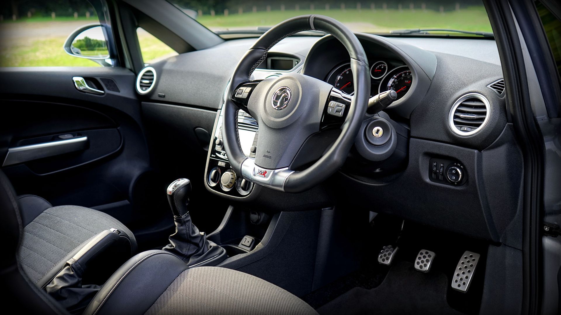 Car interior with aftermarket racing steering wheel, manual gear shift, and black patterned seats