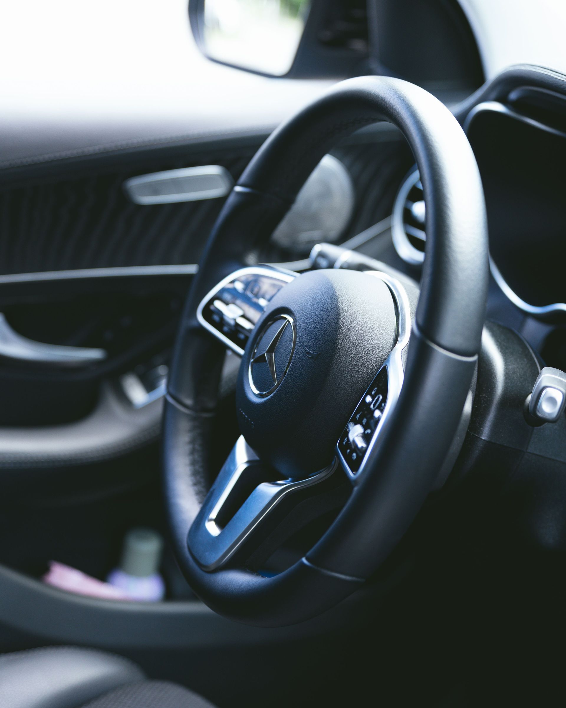 Close-up of a black steering wheel and car interior with water droplets on the wheel and dashboard.