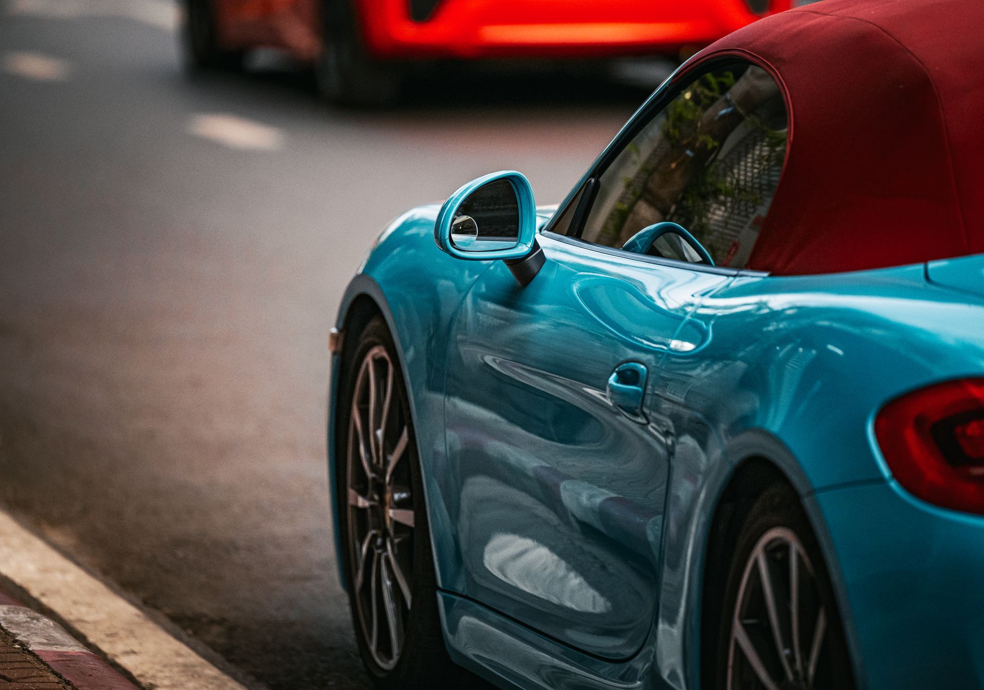Blue sports car parked on a street, seen from the side with a red car in the background