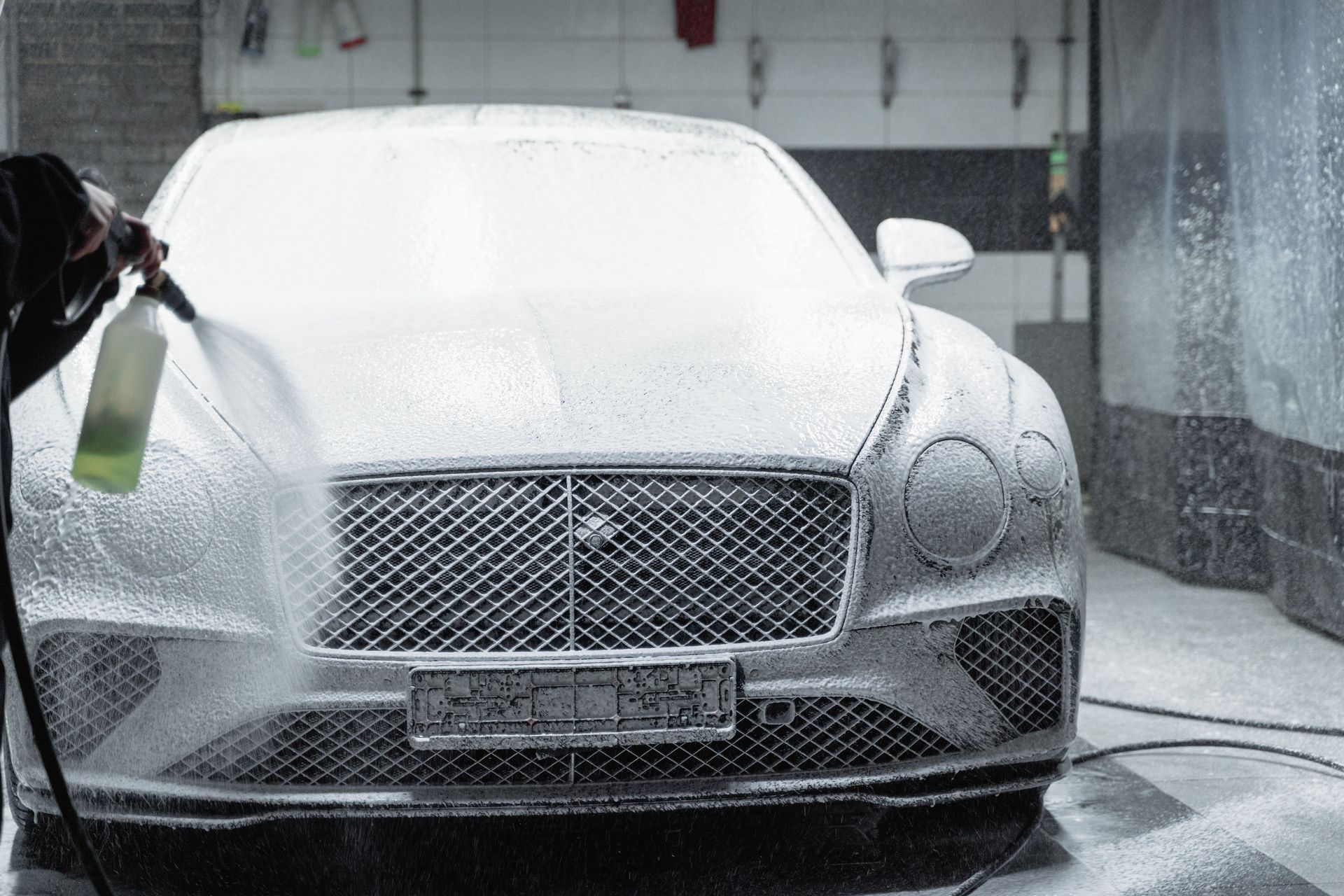 White luxury car being pressure washed in a car wash bay
