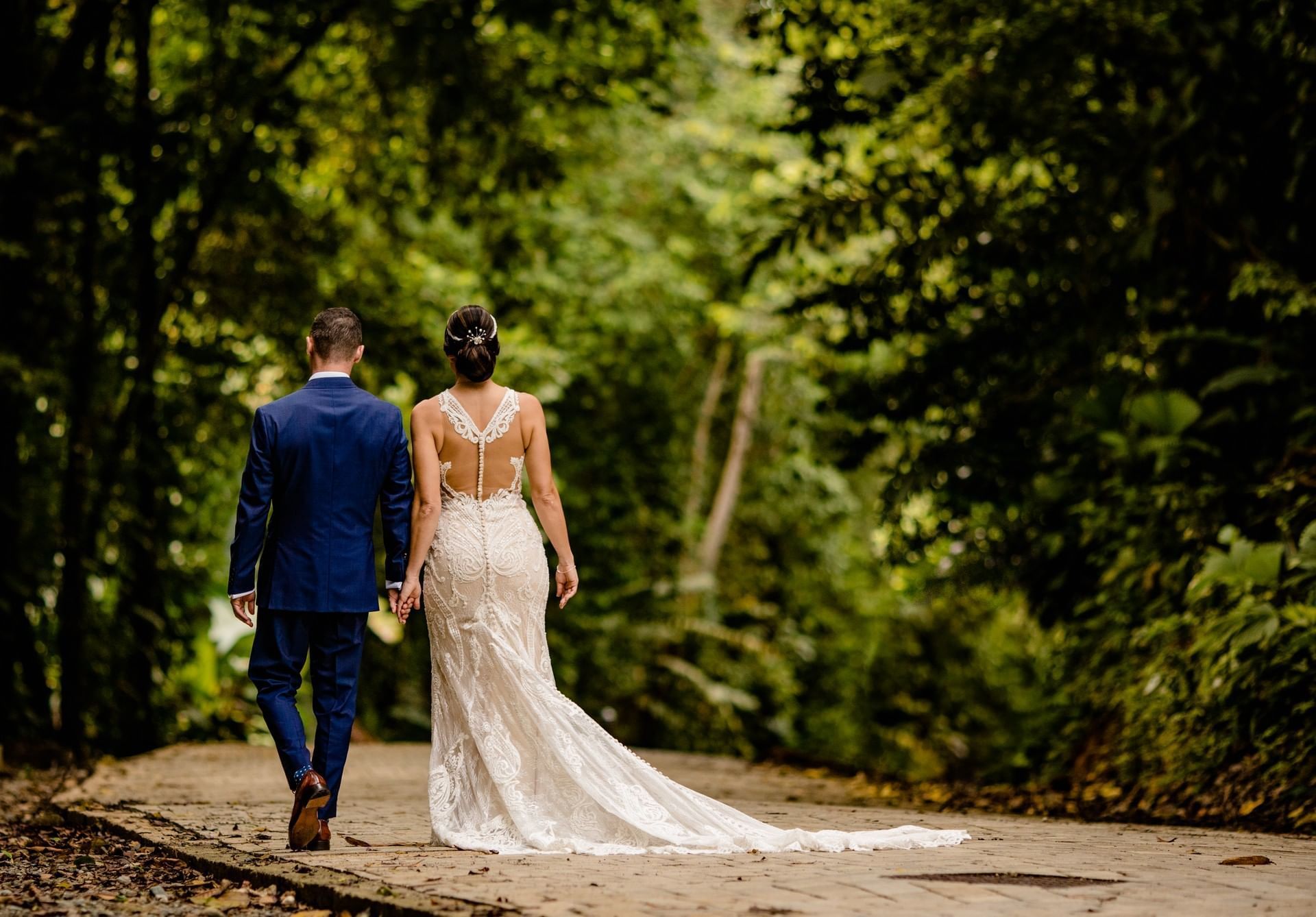 A bride and groom are walking down a path in the woods.