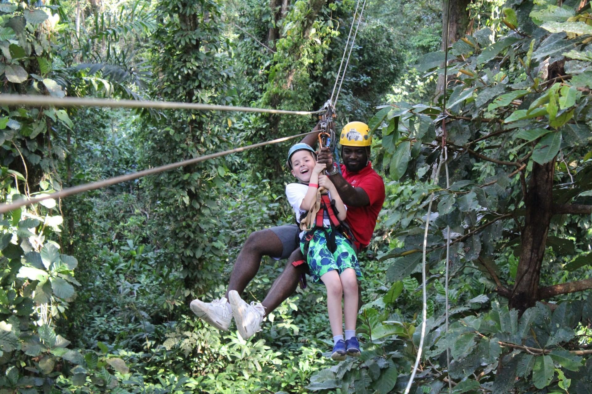 A man and a child are riding a zip line through the trees.