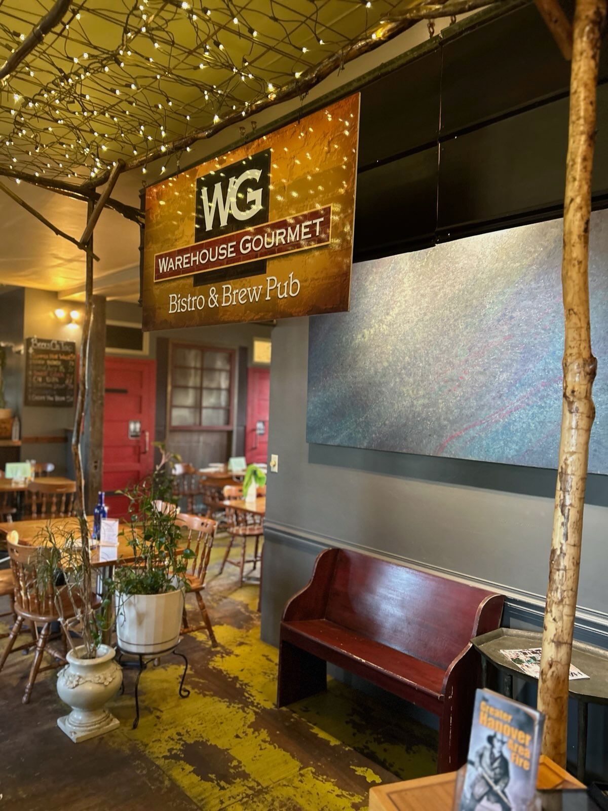 Interior view of a cozy, rustic restaurant with wooden chairs, a long booth, and a decorative fireplace mantel.