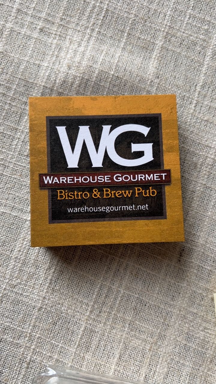 A stack of yellow Warehouse Gourmet BBQ and Brew Pub coasters sitting on a wooden table.