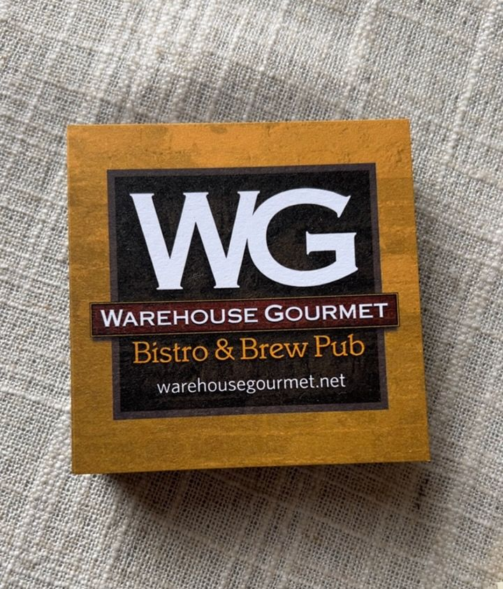 A stack of yellow Warehouse Gourmet BBQ and Brew Pub coasters sitting on a wooden table.