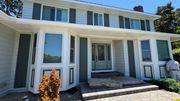 Two-story house with light blue siding, white trim, and gray shutters. A person paints on the side.