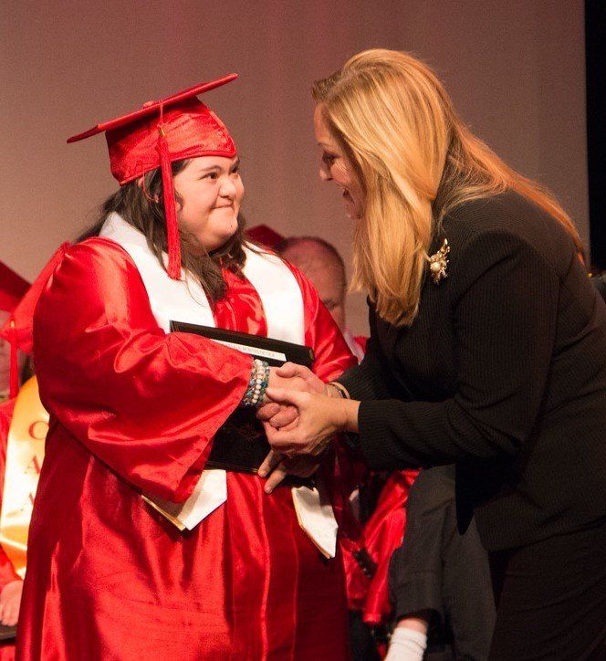 a woman in a graduation cap and gown is shaking hands with another woman