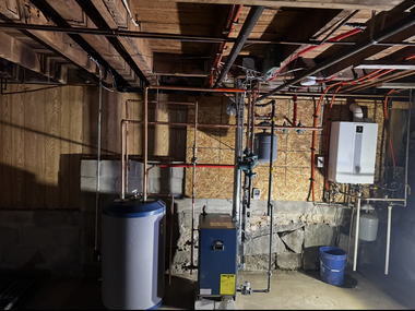 Modern blue industrial boiler system with complex copper piping installed against a concrete basement wall.
