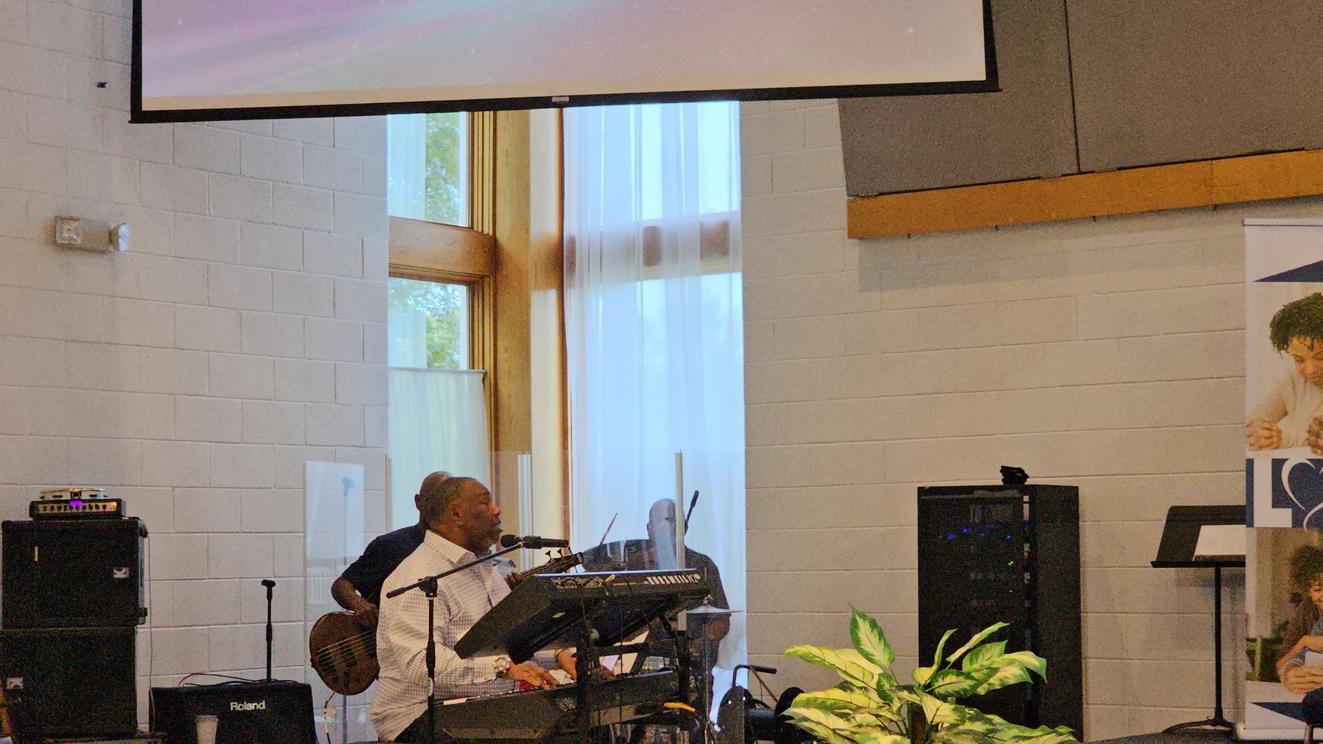 Musician at a drum kit on a church stage with a microphone and projector screen behind him
