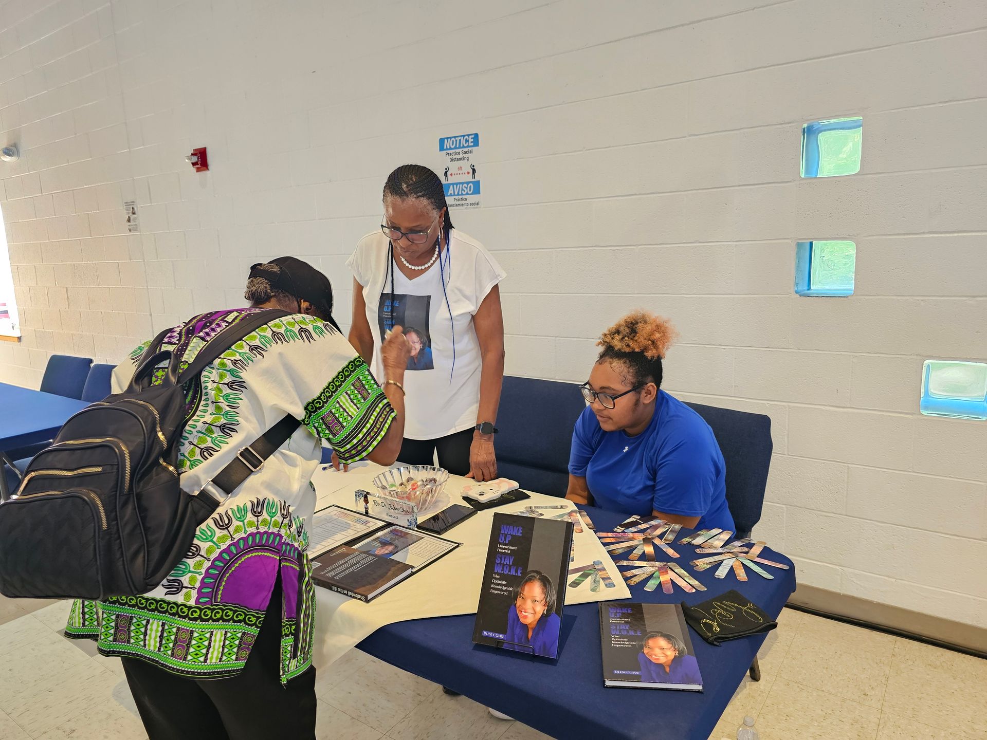 People at a table in a hallway, discussing brochures and a photo display at a community event.