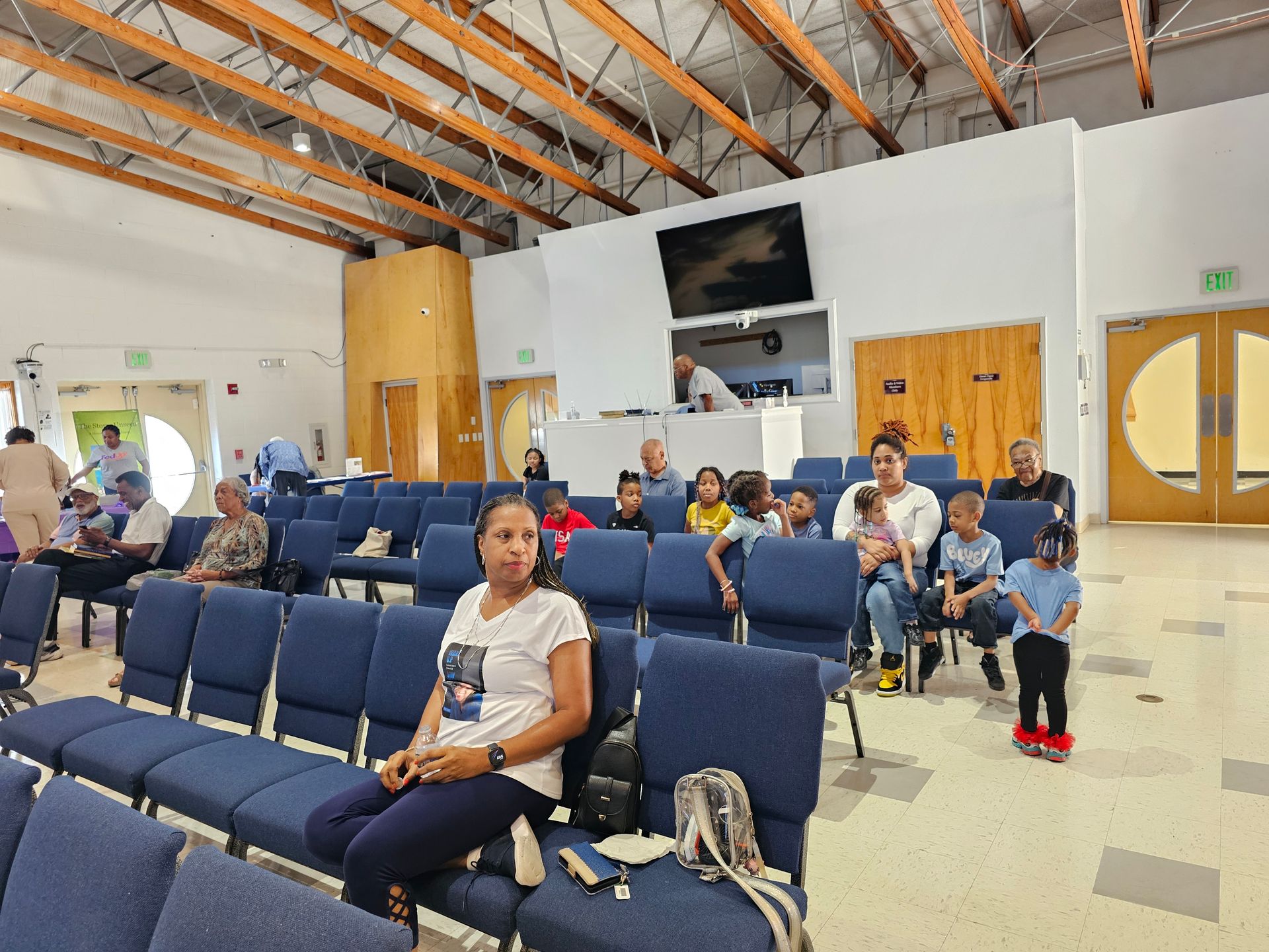 People seated in a bright waiting area with blue chairs and wooden doors.