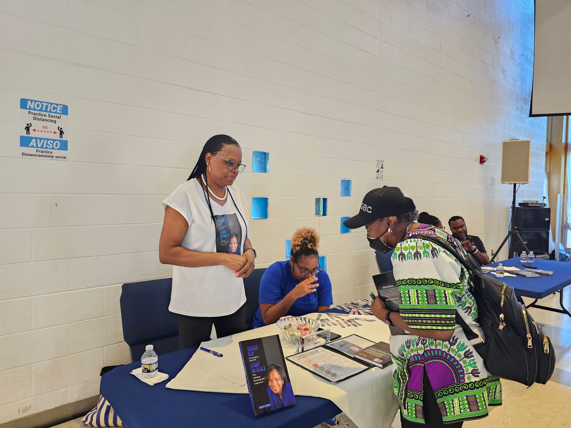 People at a table in a community room, with a laptop, papers, and books on display.