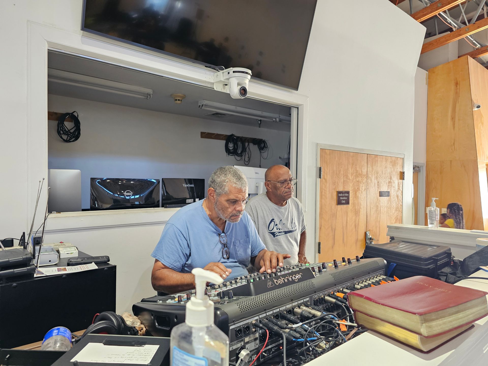 Two people at a sound mixing console in a studio, surrounded by equipment and cables.