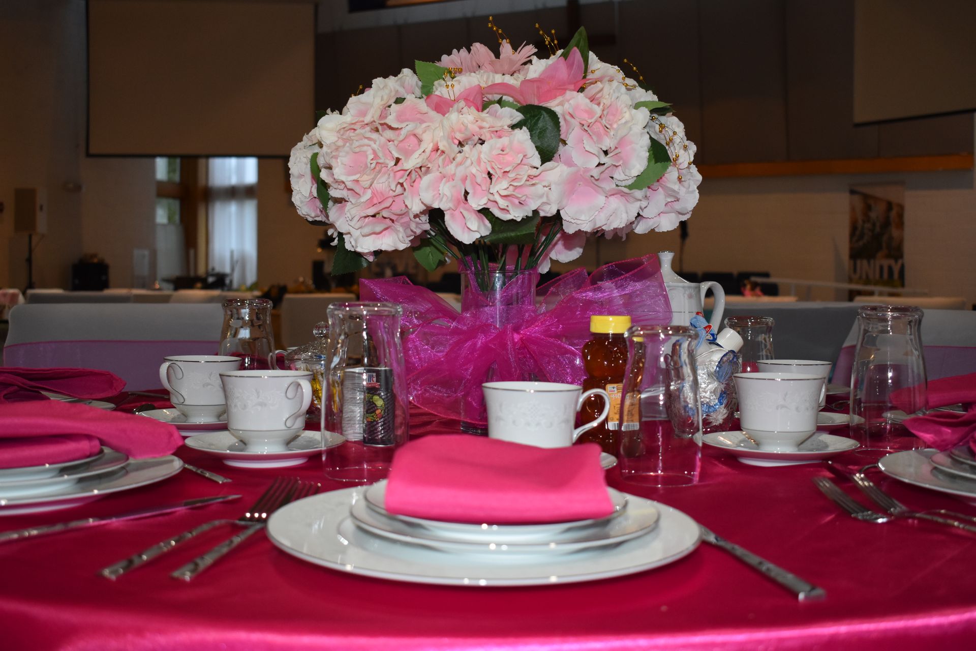 Elegant banquet table with pink tablecloth, white dishes, and a pink-and-white floral centerpiece