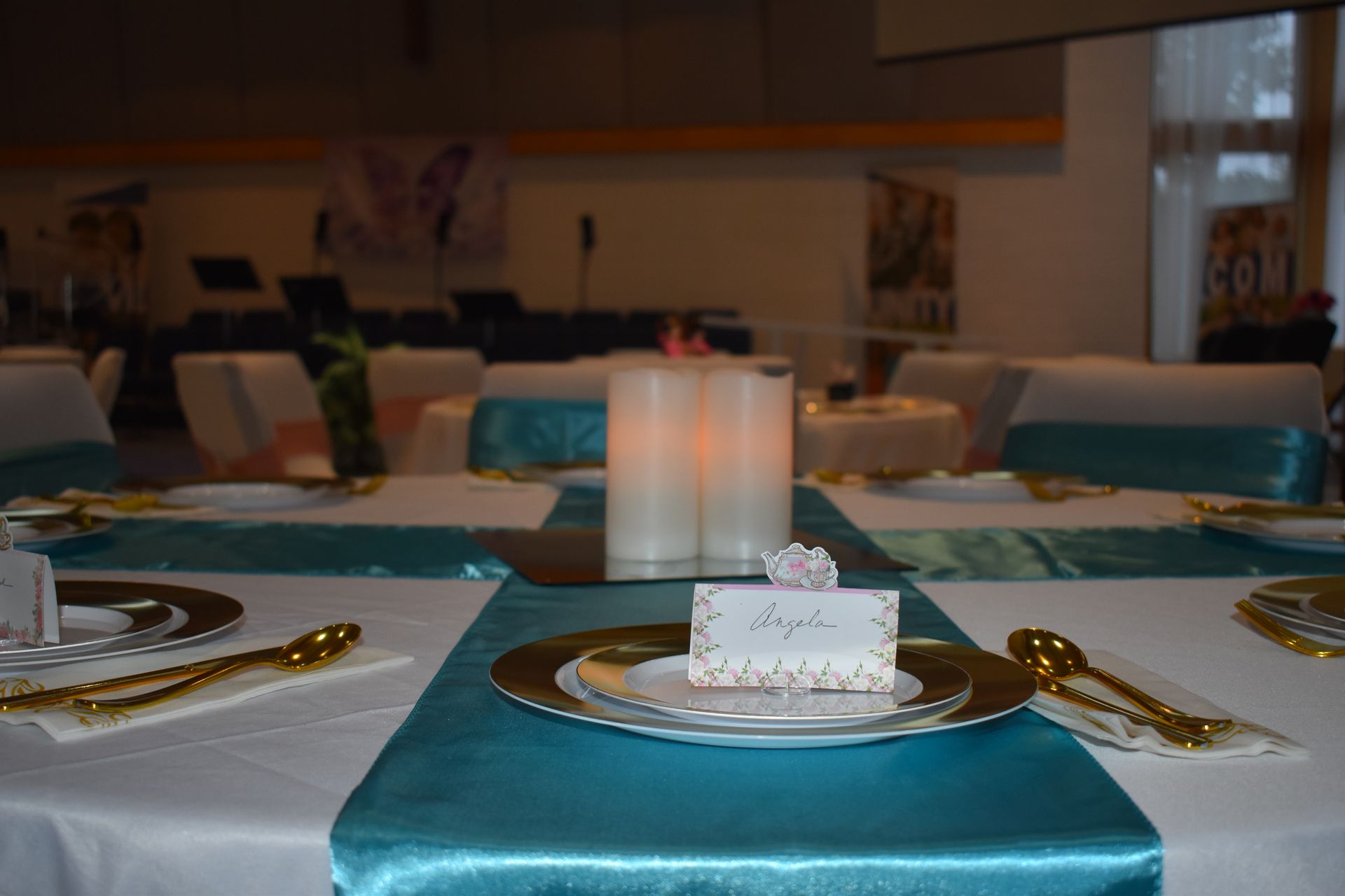Elegant banquet table with teal runners, gold plates, and candle centerpieces in a softly lit dining room