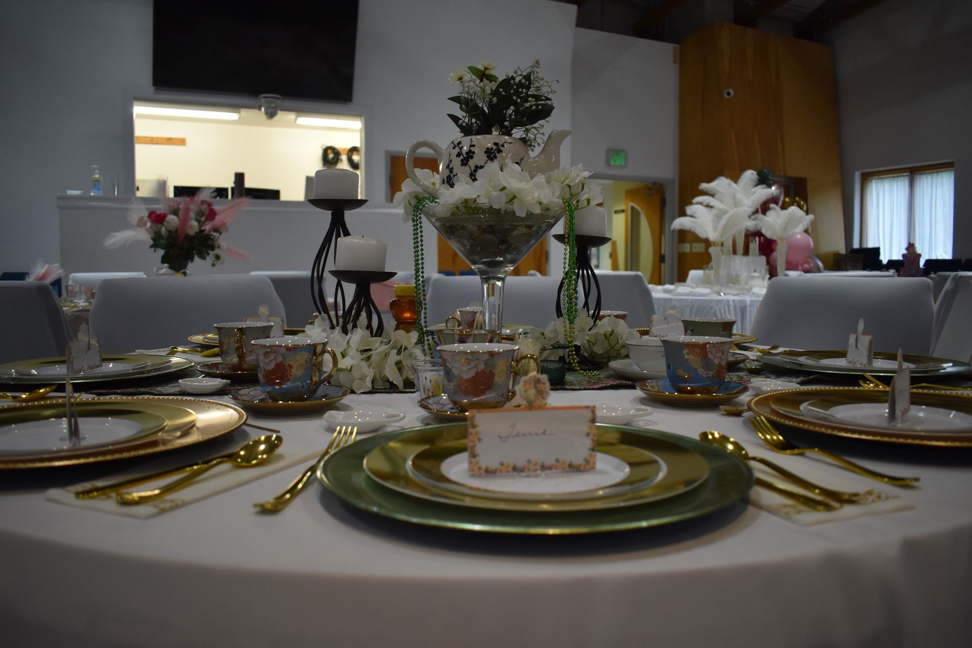 Elegant dining table set with gold accents, floral centerpieces, and place settings in a modern event venue