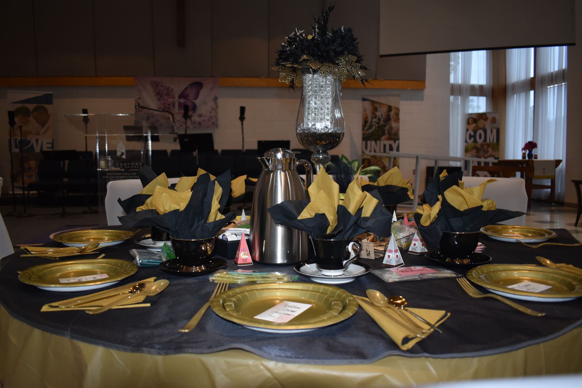 Formal dining table set with black and gold place settings and silver centerpieces in a banquet hall