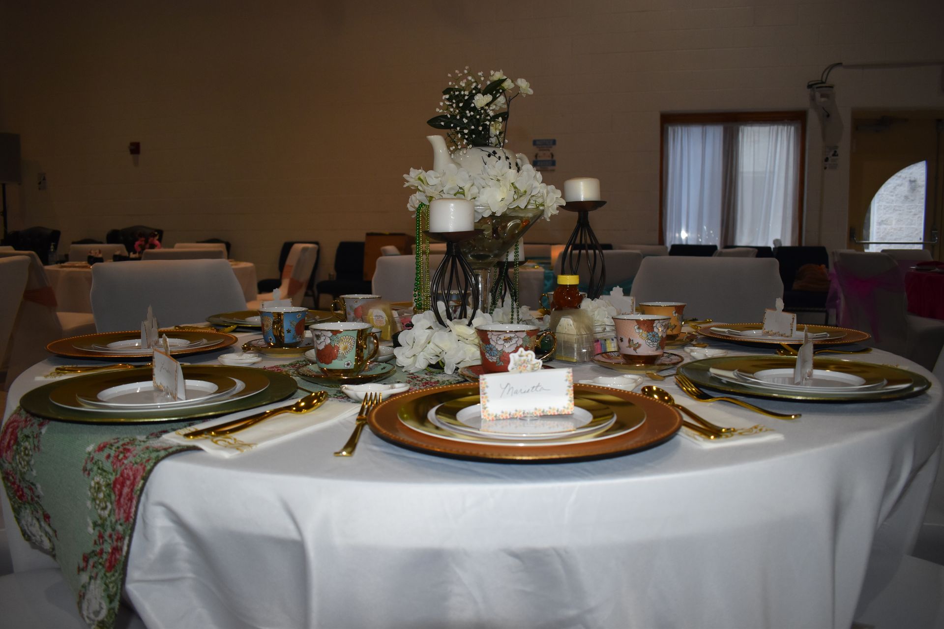 Elegant banquet table with white tablecloth, gold-rimmed plates, and floral centerpiece in a dim room