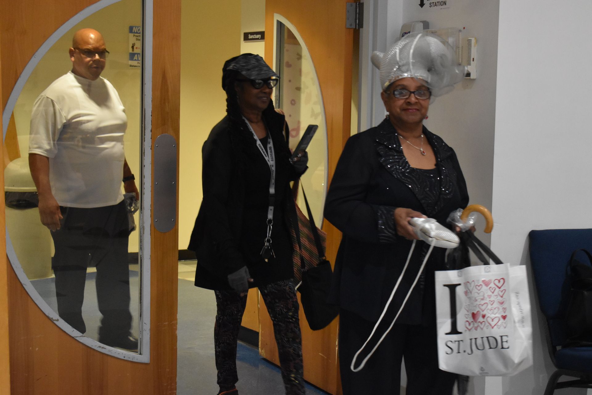 Three people walk through a doorway in a hallway, one carrying a white shopping bag.