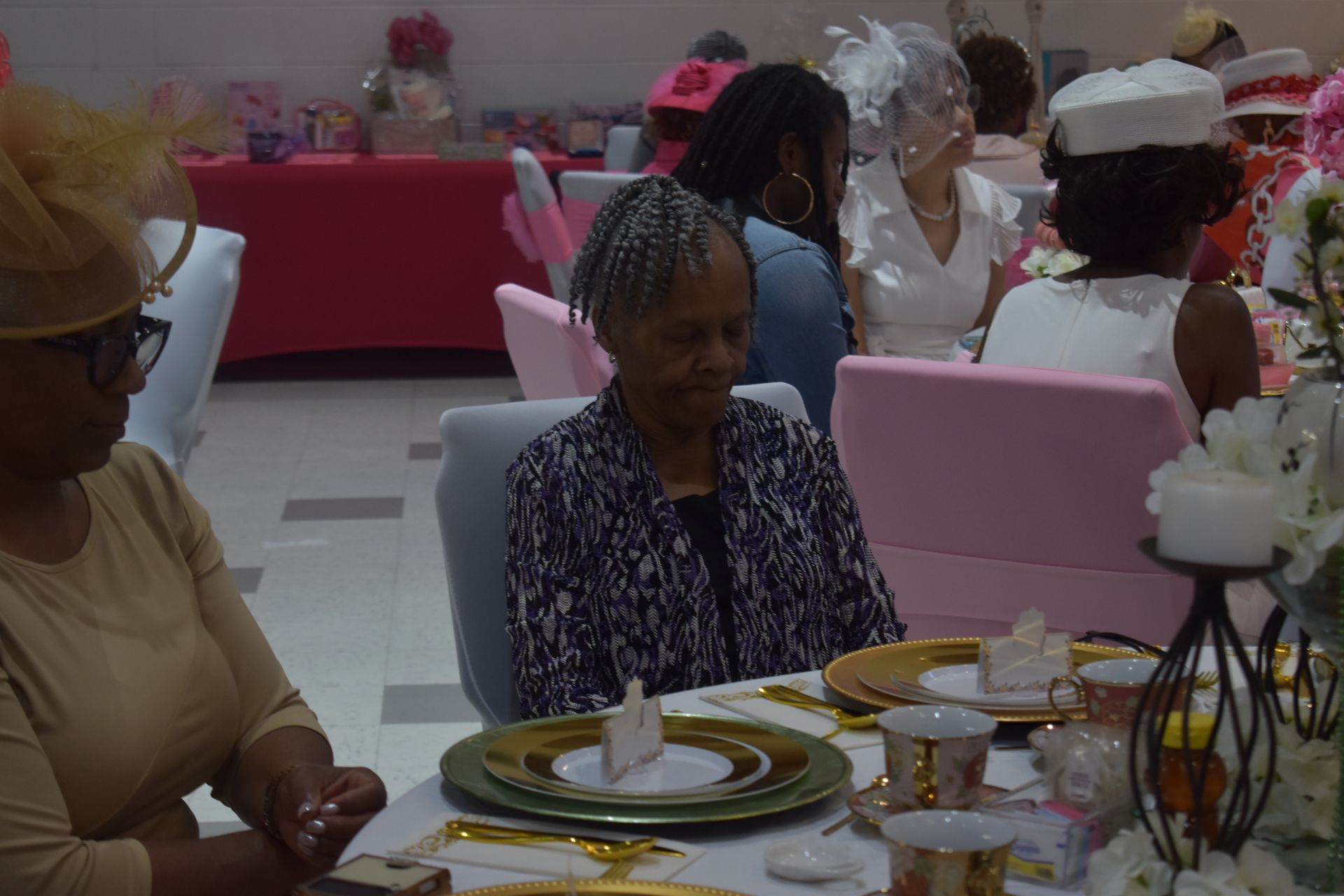 People seated at a decorated banquet table with pink chairs and floral centerpieces