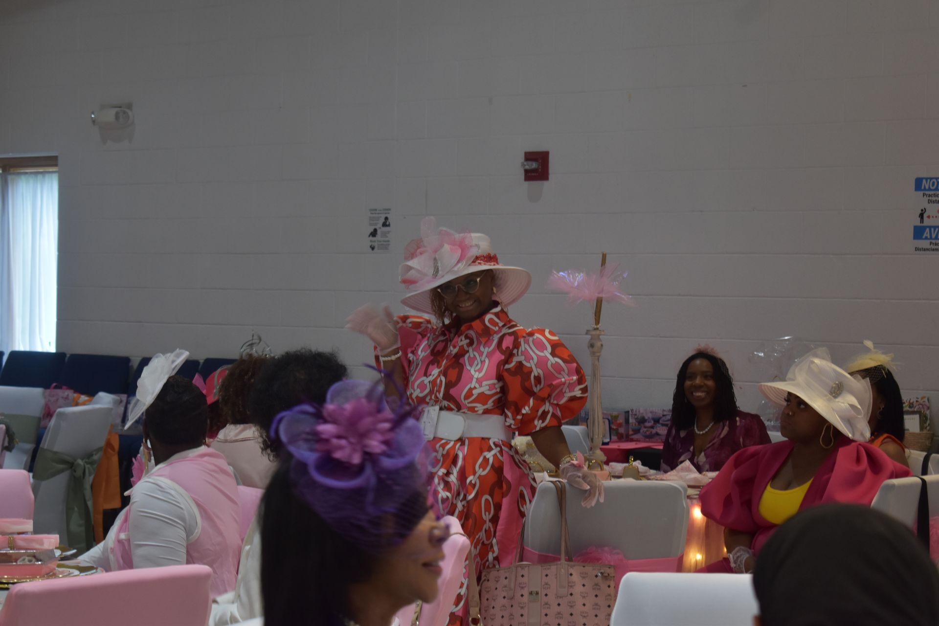 Person in red floral dress and hat performing at a decorated indoor event with seated audience