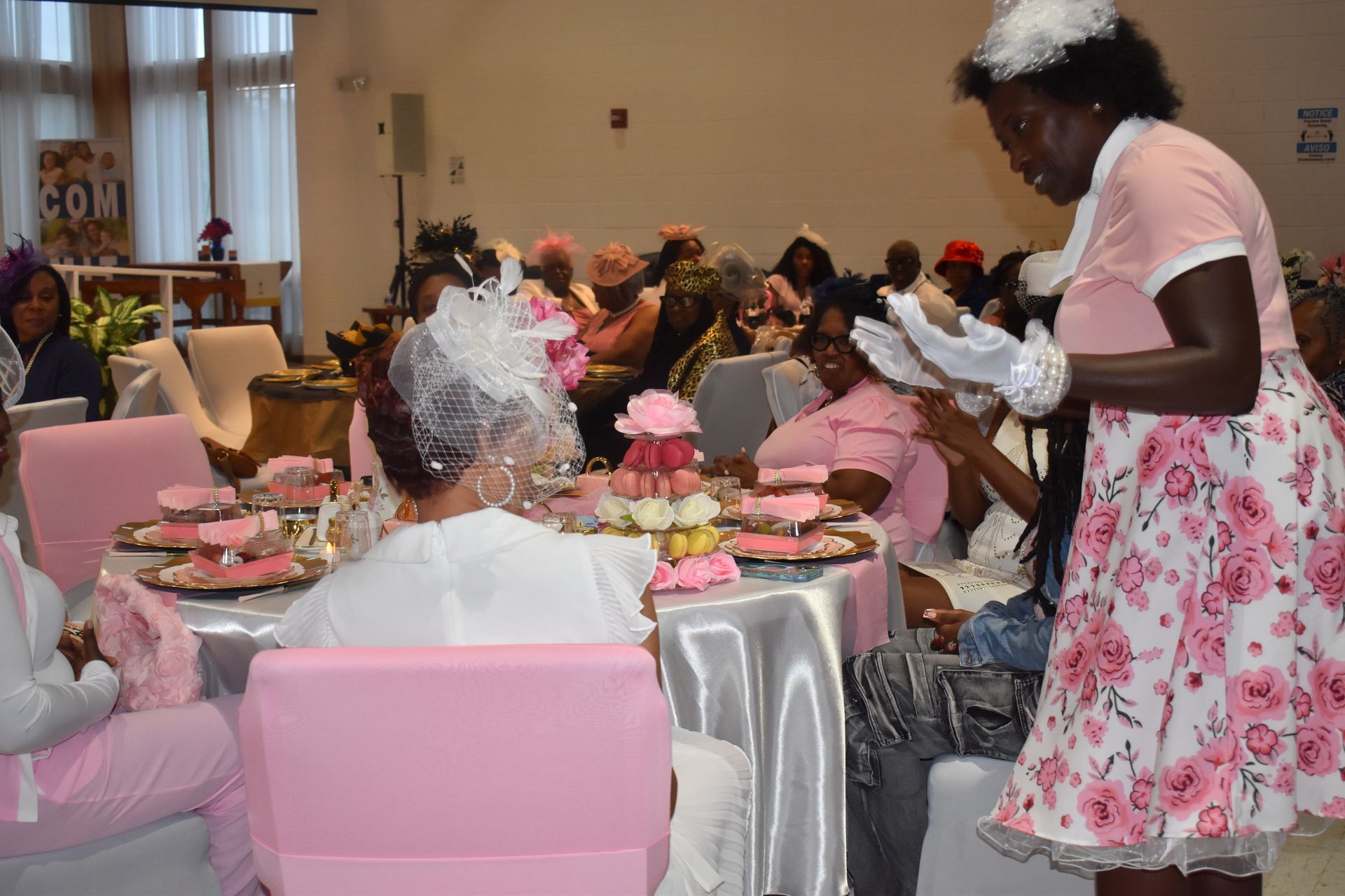 Decorated banquet hall with people seated at pink tables while a server in floral dress serves food