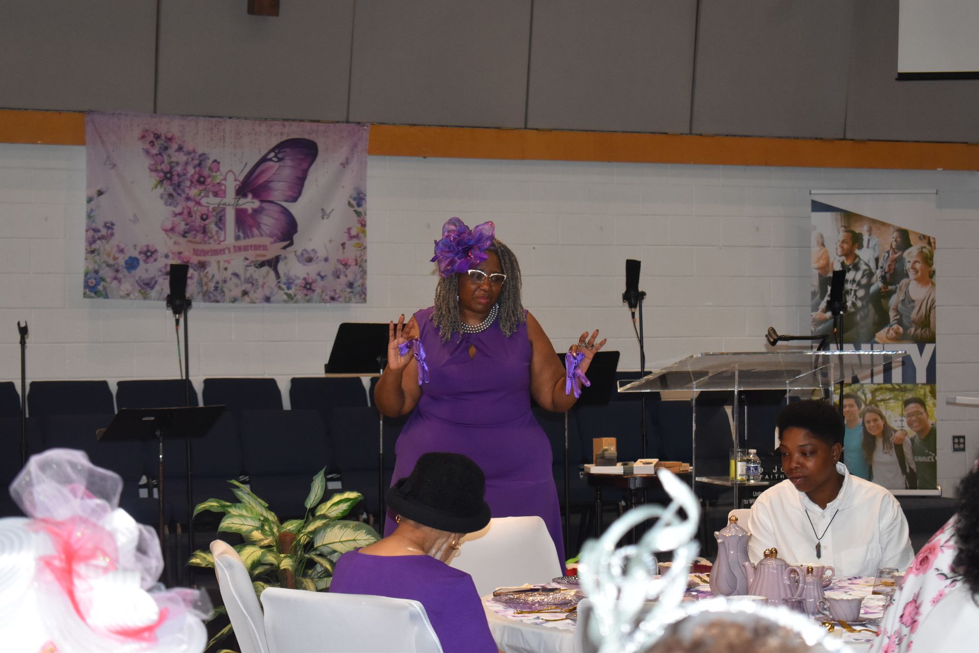 Person in purple speaking at a decorated church event with seated attendees nearby