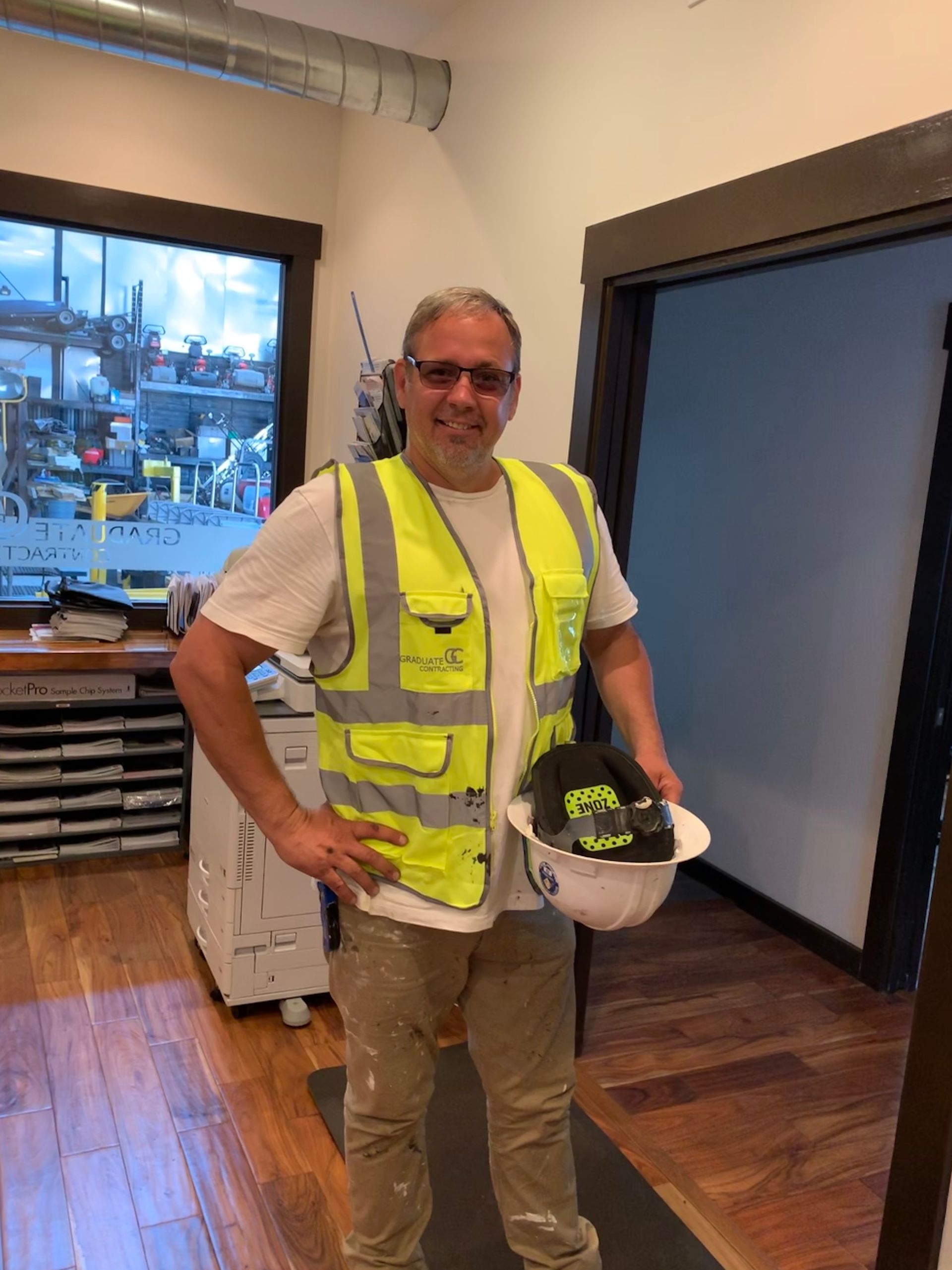 A man wearing a yellow vest and holding a hard hat is standing in a room.