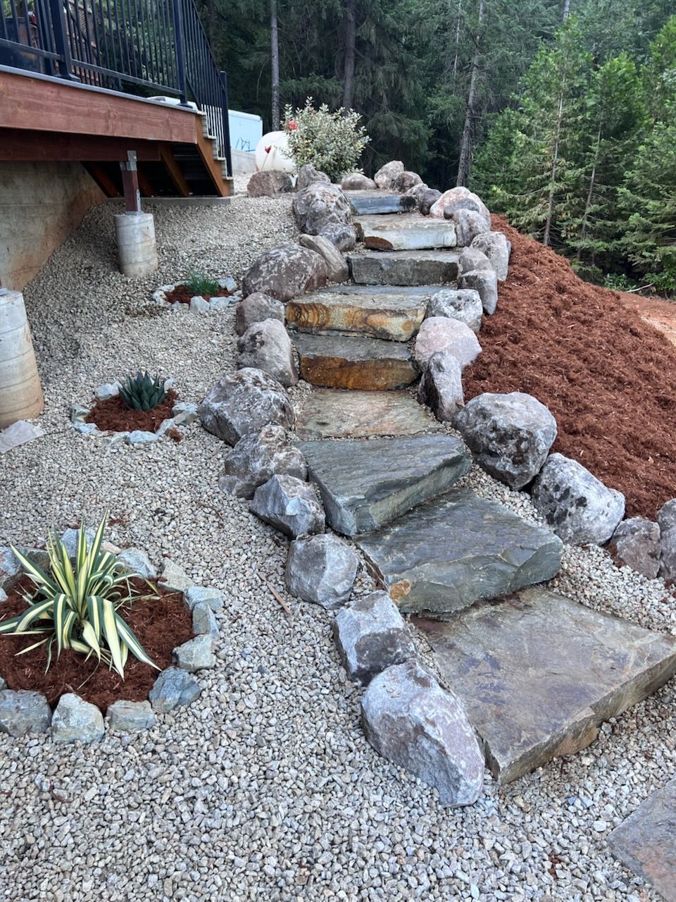Natural stone steps leading up a hillside beside a gravel garden bed and wooden deck.