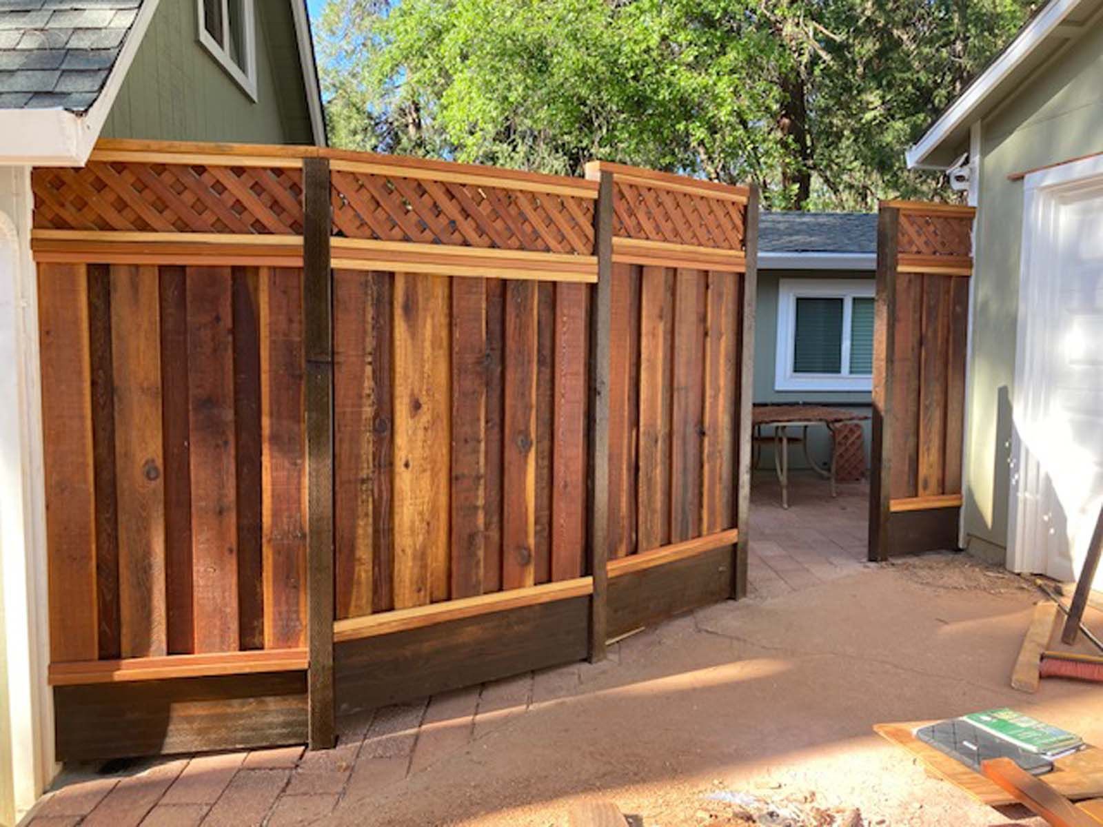 A newly installed cedar wood fence with a lattice top and dark-stained base panels stands between two houses.