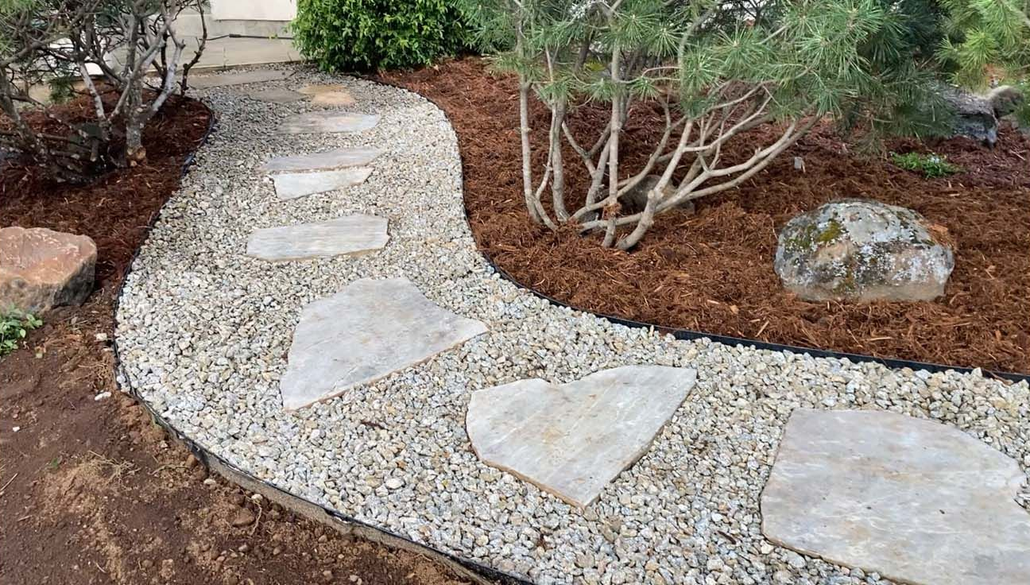 A winding garden path made of irregular stone stepping stones set in light gravel, bordered by dark mulch and shrubs.