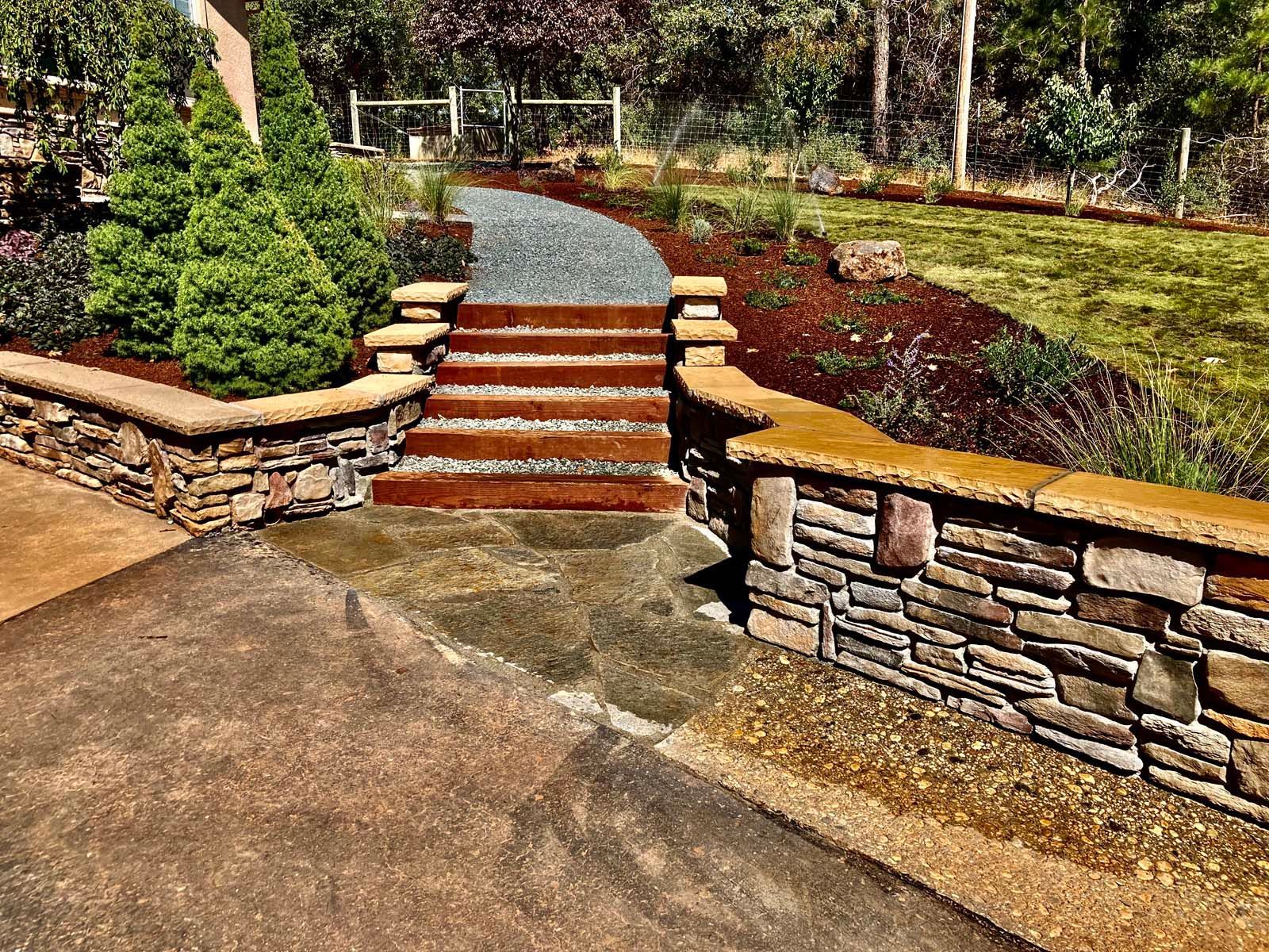 Stone steps with metal risers leading up a path between two stone retaining walls in a landscaped garden.
