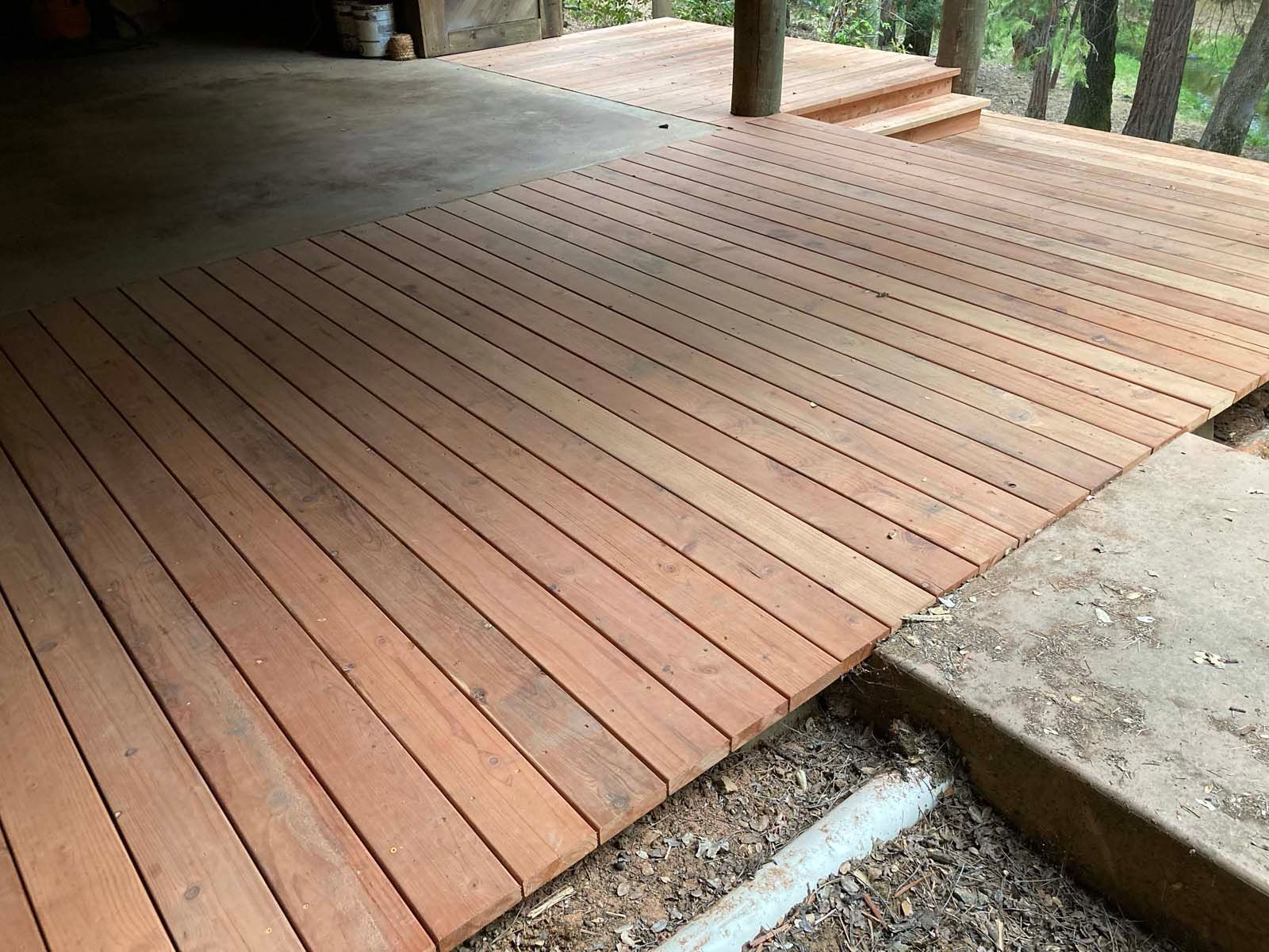 A newly built wooden deck extends from a concrete patio, transitioning into steps leading toward a wooded area.