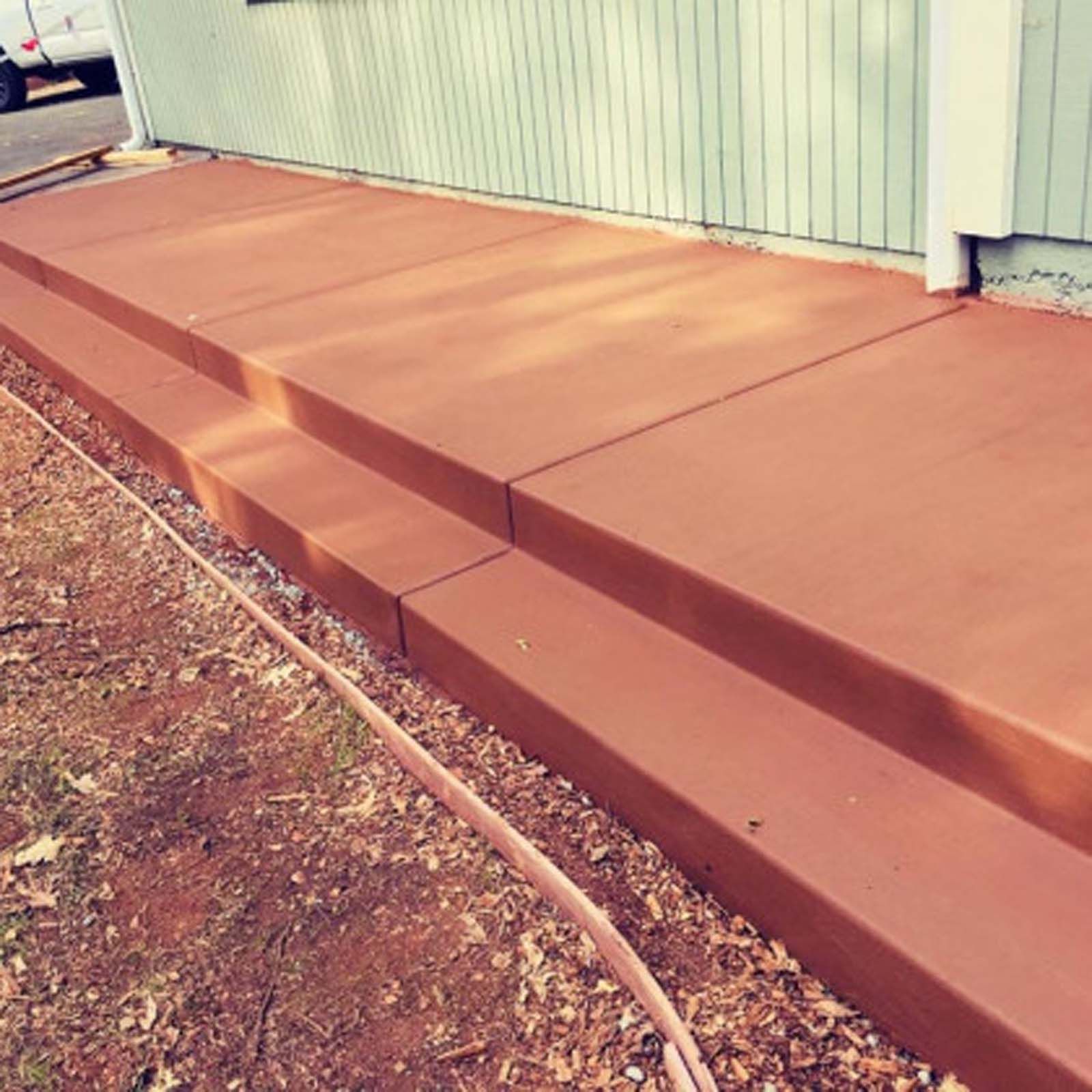 A freshly poured, smooth, reddish-brown concrete patio or set of stairs attached to a light green house.