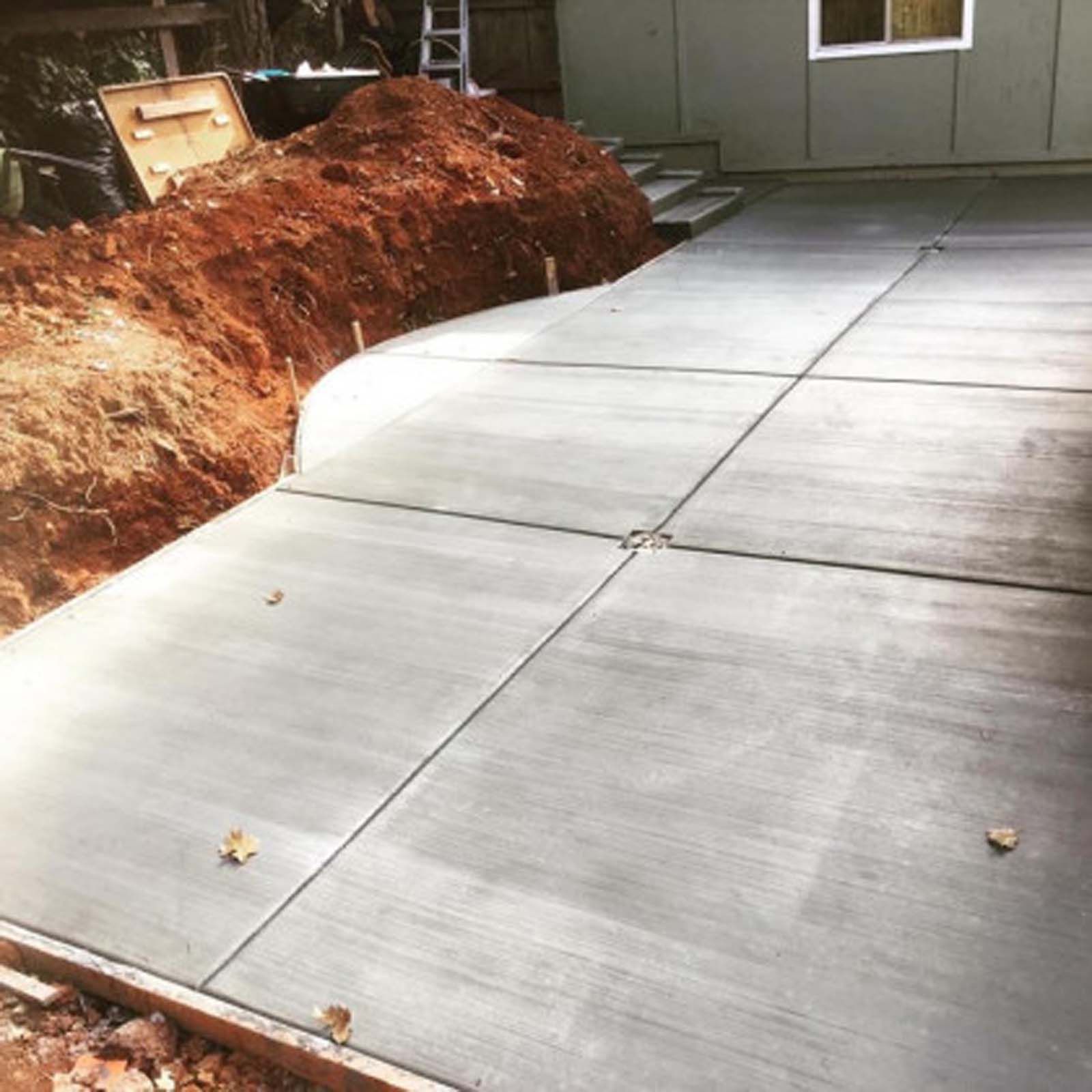 Newly poured concrete patio next to a pile of dirt and a house exterior.