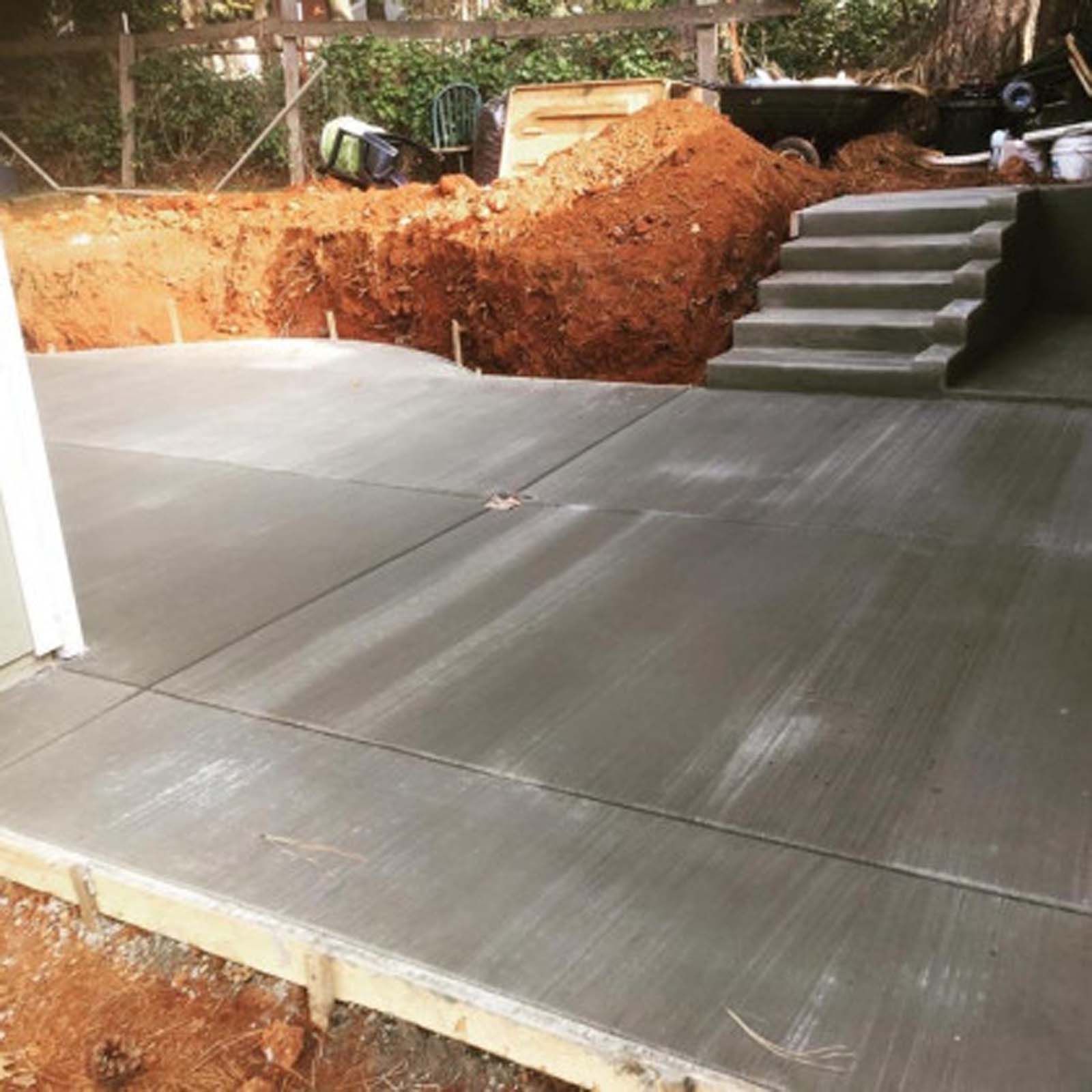 A freshly poured gray concrete patio with stairs leading up to an unlandscaped dirt embankment.