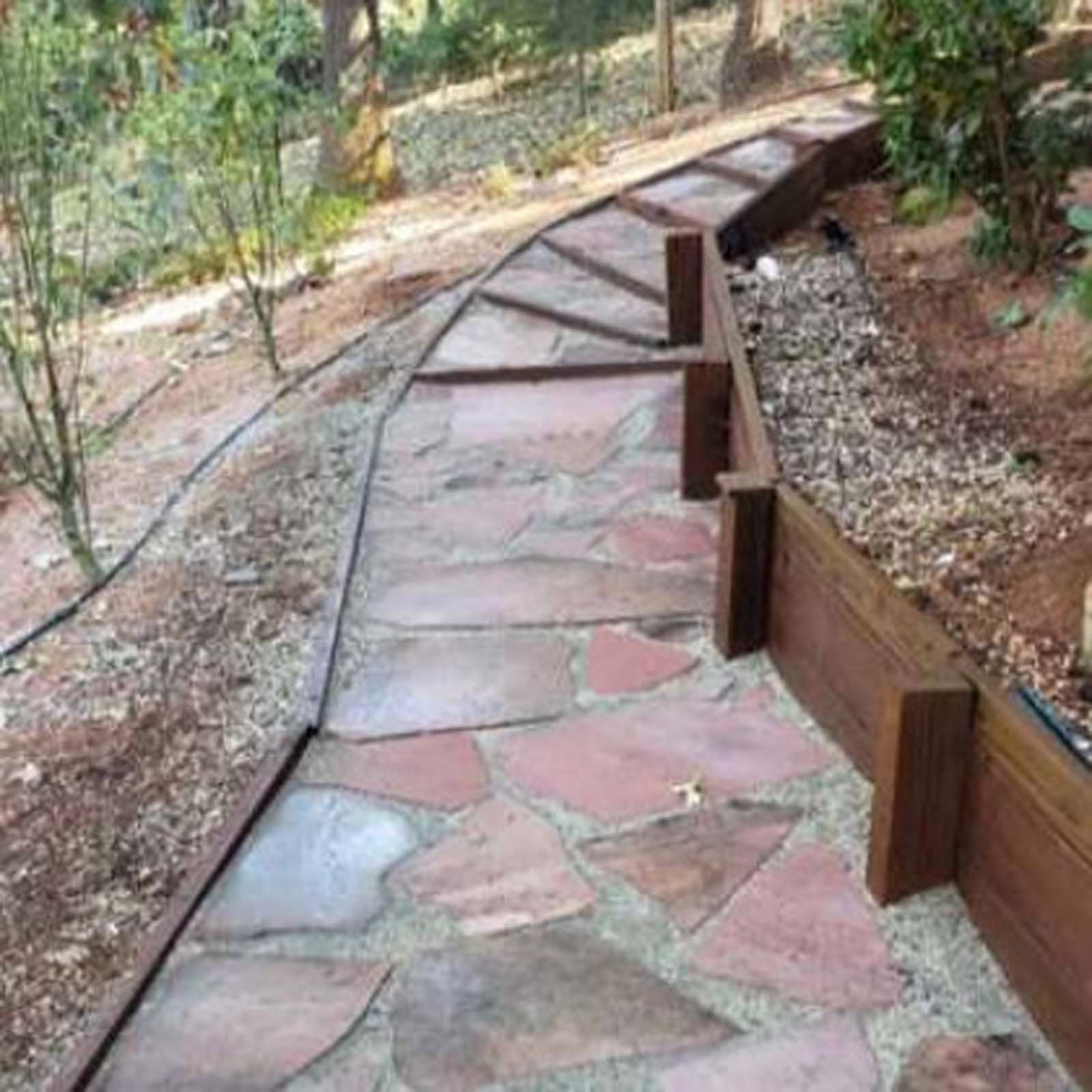 A curving flagstone path winds uphill, bordered by wooden retaining walls and gravel on a dirt slope.
