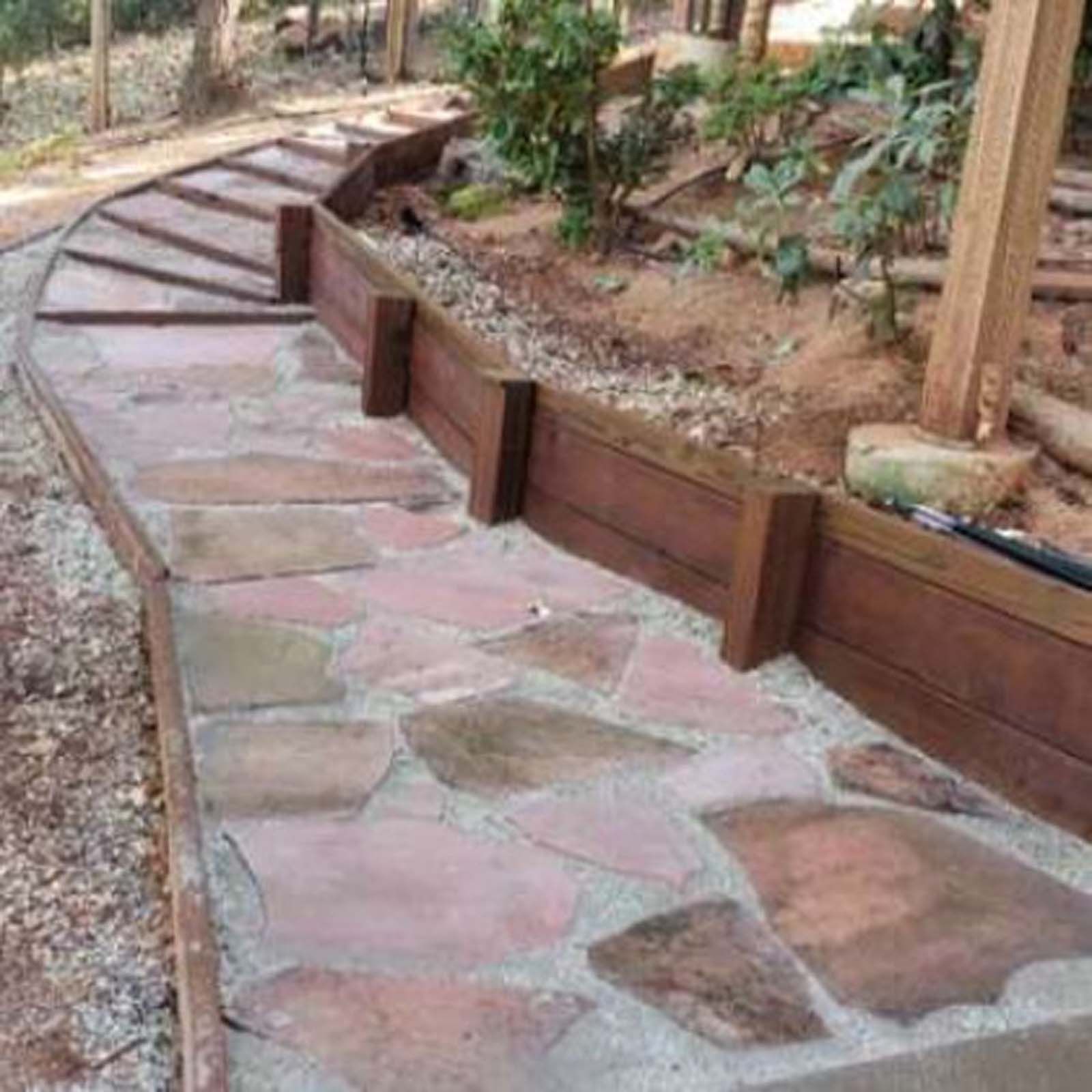 A stone pathway with wooden retaining walls curves uphill through a garden setting.