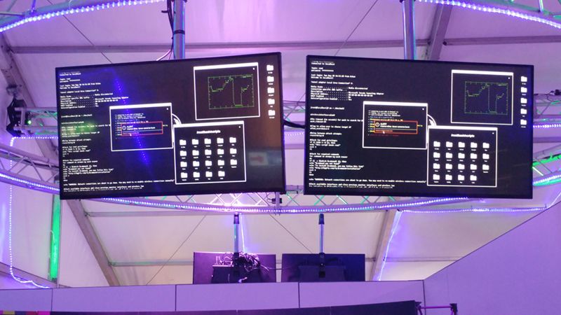 two monitors are hanging from the ceiling in a room with purple lights .