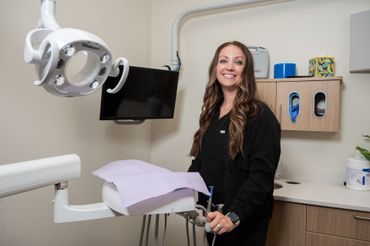 Dentist smiling in a dental office next to the patient's chair and tools.