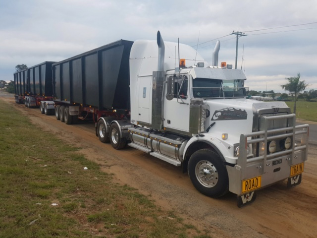 White semi-truck with multiple black cargo trailers on a dirt road — Chewies Tipper Hire & Haulage in Gracemere, QLD