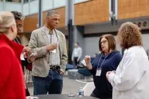 Four people stand in an indoor atrium, engaged in a discussion around a table.