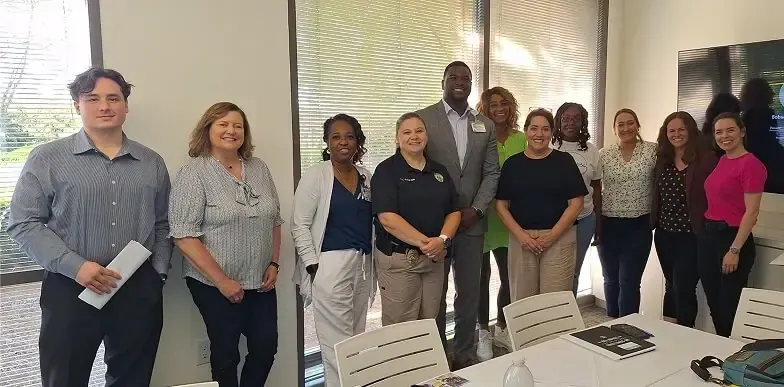 A diverse group of eleven people standing and smiling together in a brightly lit office space.