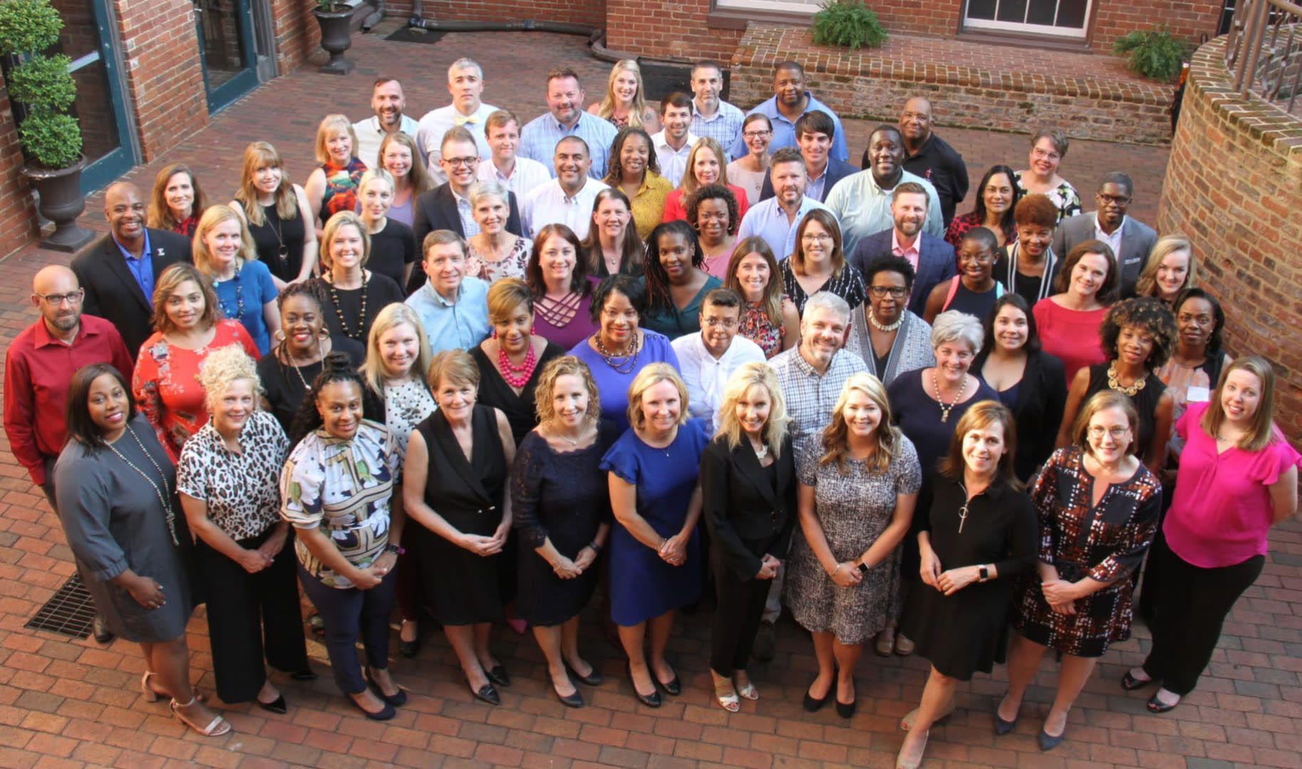 A large group of people stand together smiling on a brick patio for a formal team photo.