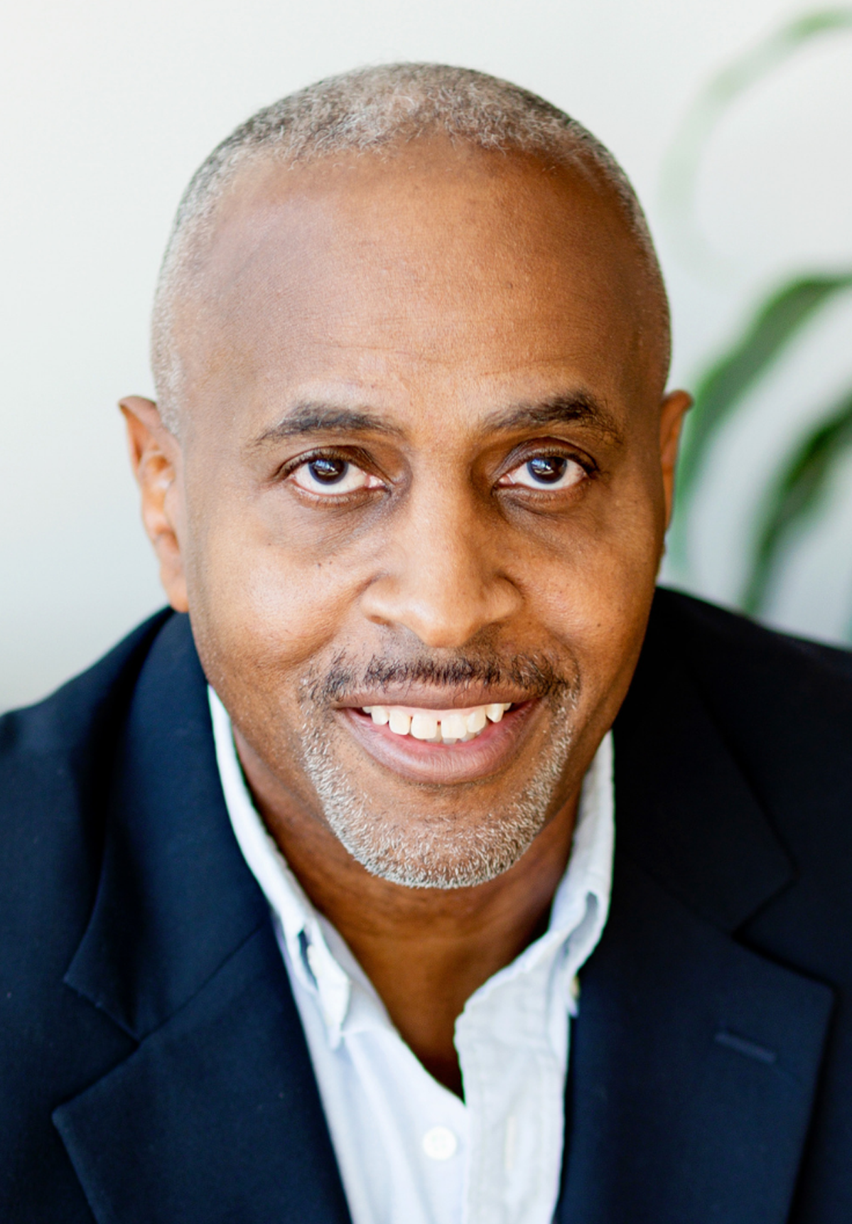 Head-and-shoulders portrait of a smiling man in a dark blazer and white shirt on a light background