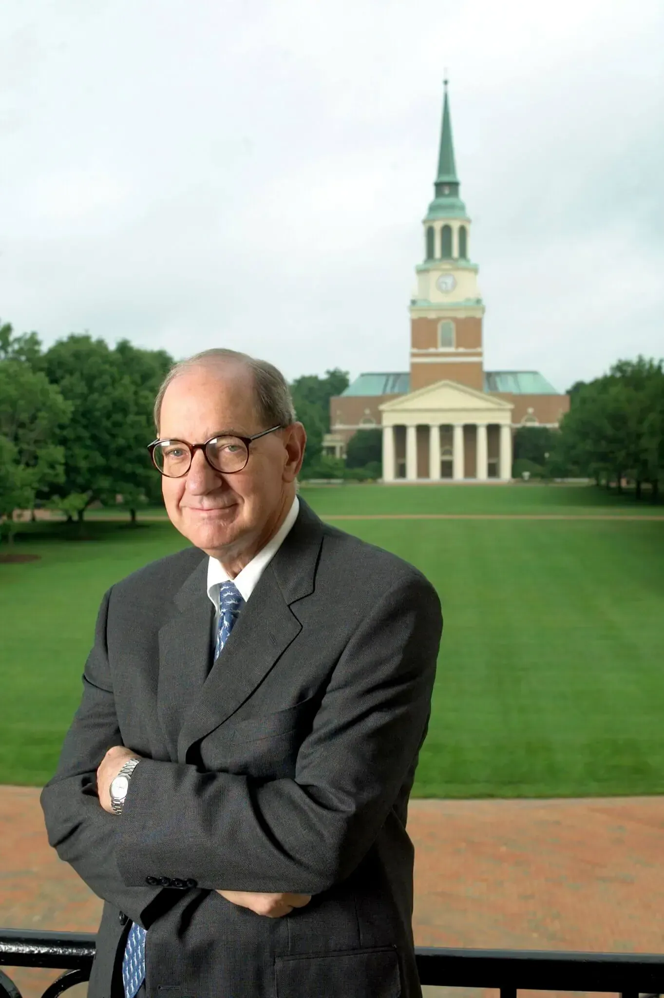 A person in a suit stands with arms crossed before Wait Chapel on the Wake Forest University campus.