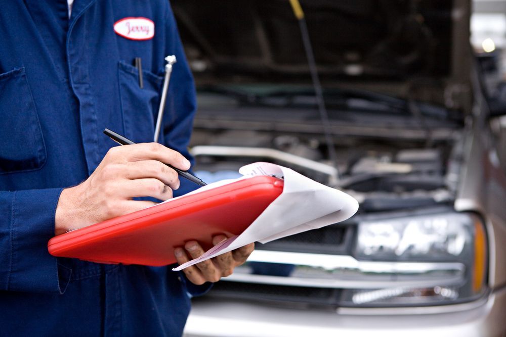 Mechanic In Blue Overalls With Clipboard Inspecting Car Engine — Britek Automotive in Bentley Park, QLD