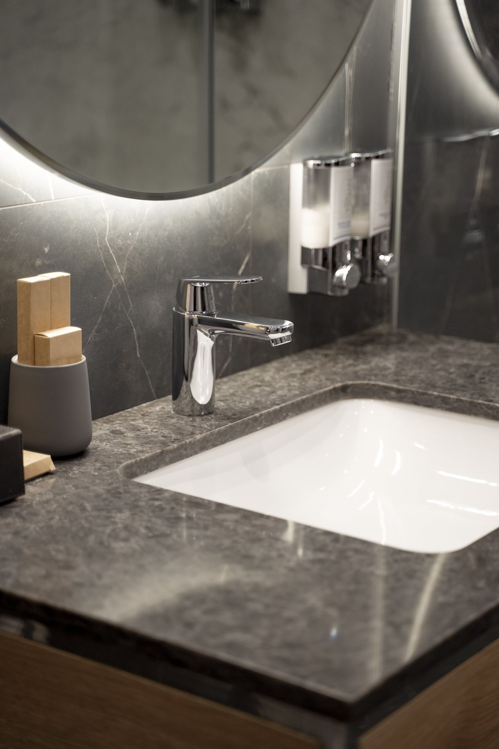 A bathroom with a sink , mirror and soap dispensers.